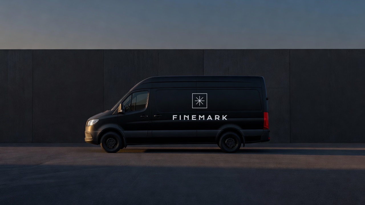 A black work van lettered with the Finemark mark and wordmark, parked against a concrete wall at dusk